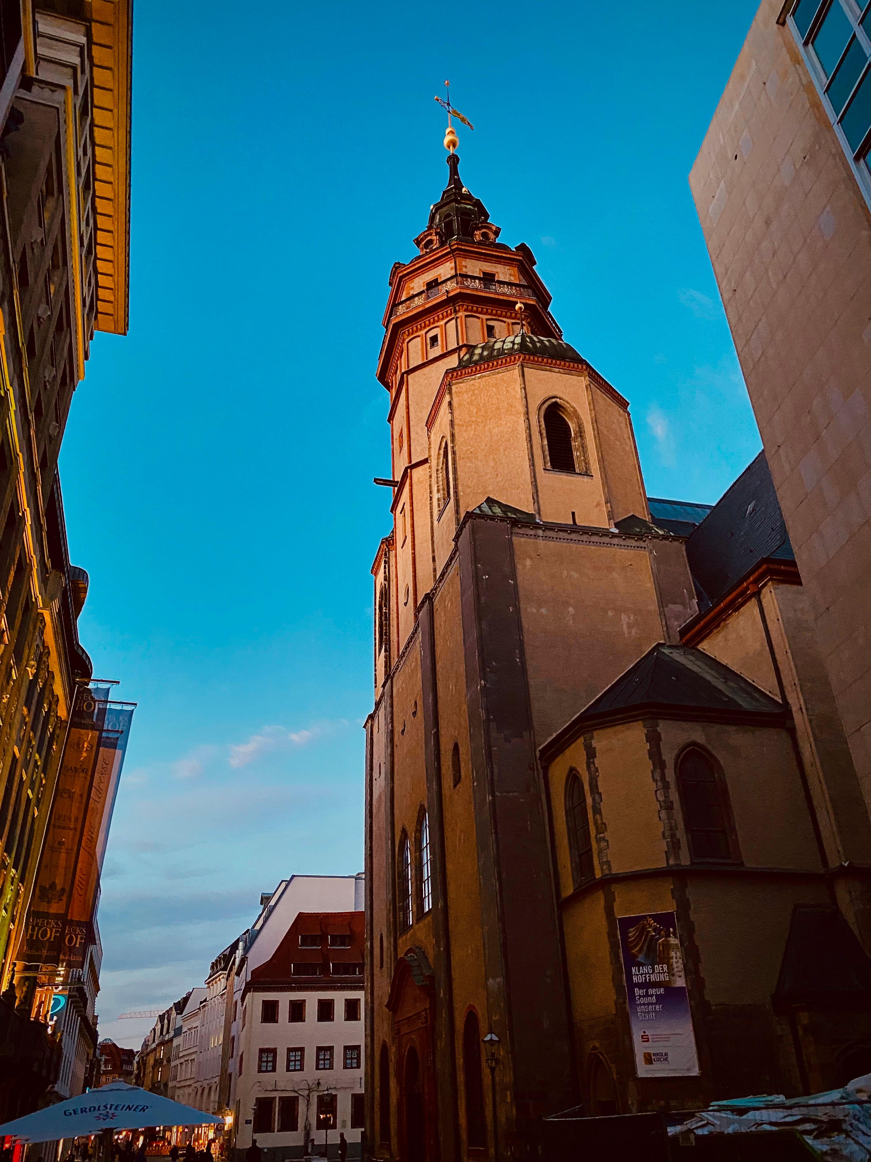 Baroque church tower rising above a pedestrian street at dusk