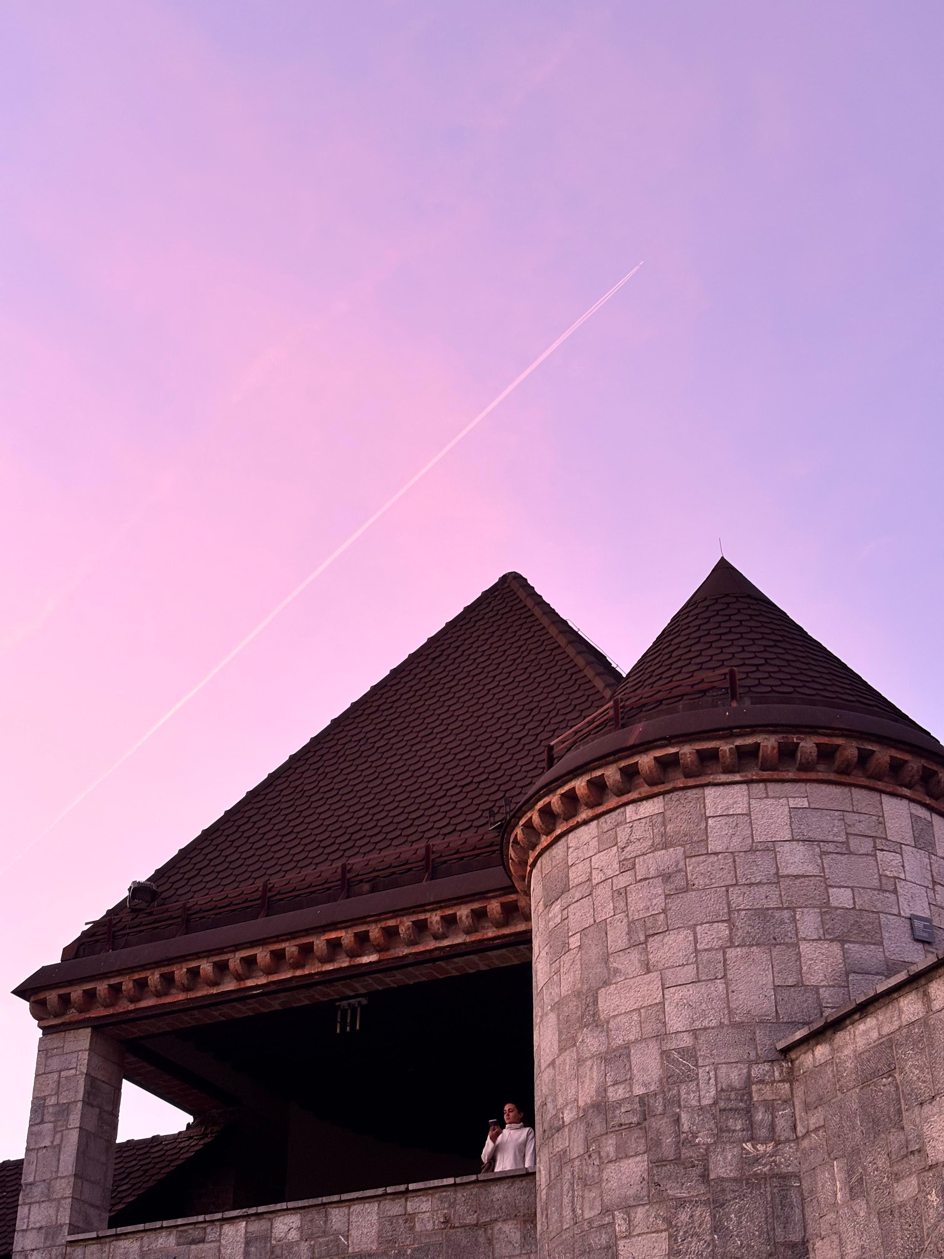 Ljubljana Castle tower against a pink evening sky with a contrail
