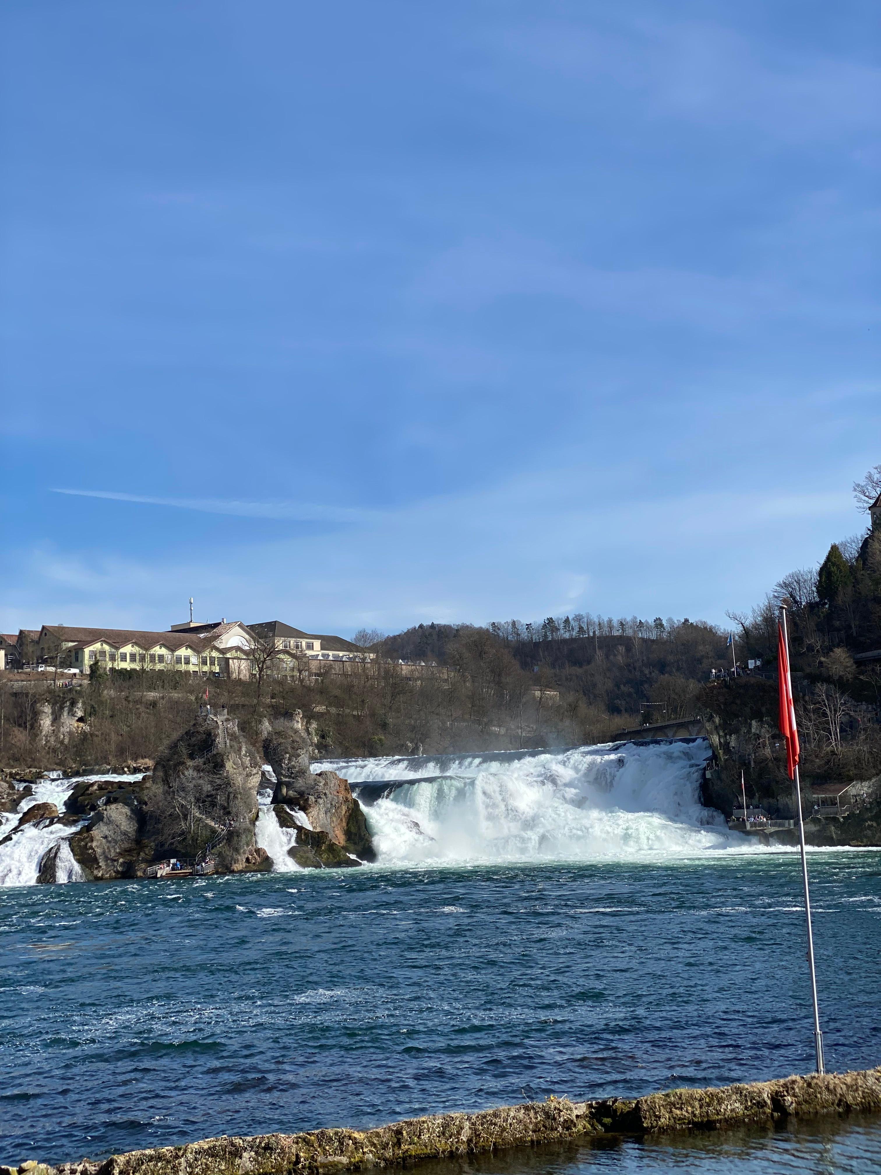 Rhine Falls rushing over rocks with a Swiss flag in the foreground
